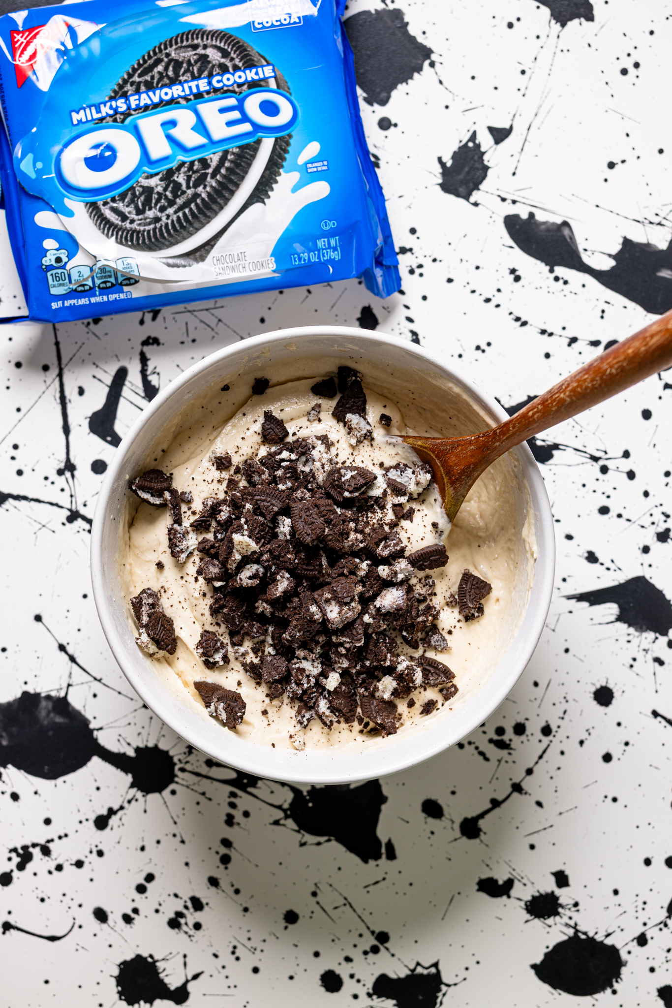 Cake batter in a bowl with crushed Oreo cookies on a white and black table.