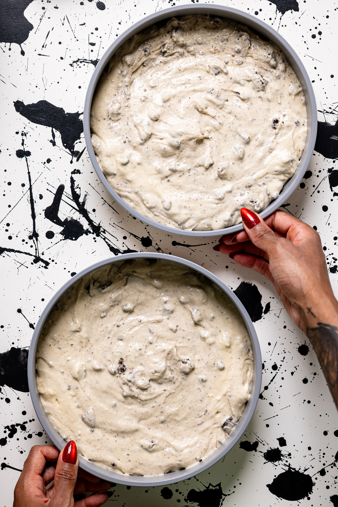 Two cake pans with batter being held by women hands.