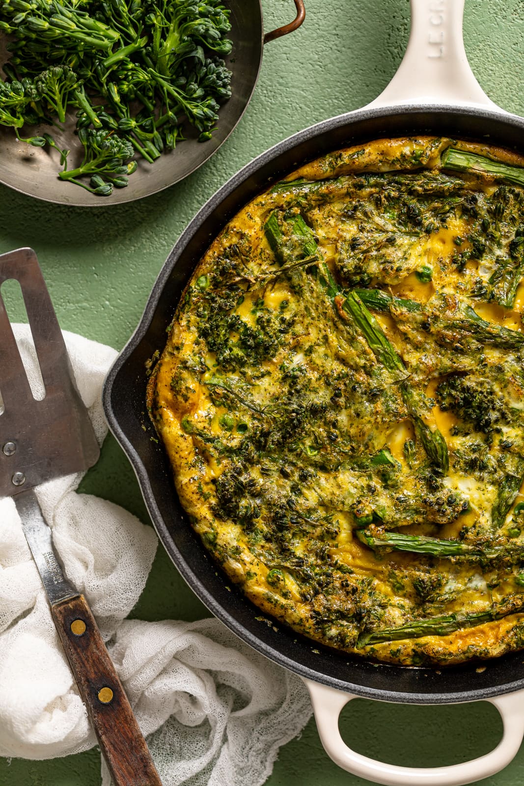 Metal spatula next to a Spring Vegetable Frittata in a skillet