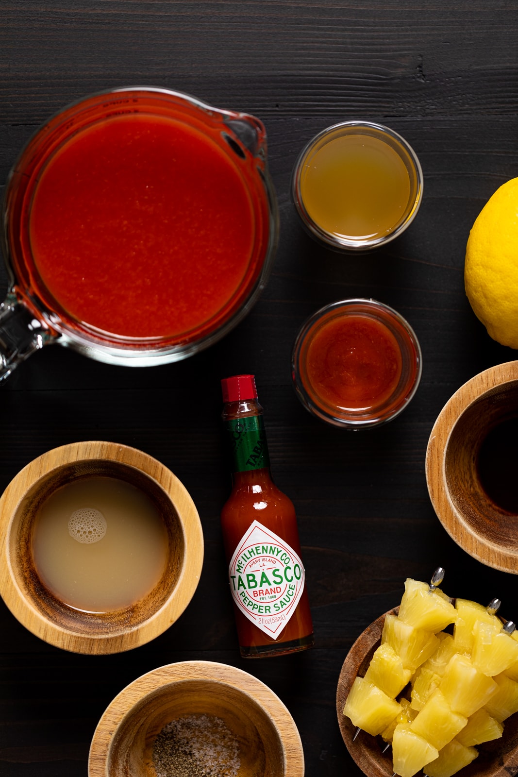 Ingredients for Bloody Mary Mocktails including Tabasco sauce, pineapple chunks, and spices