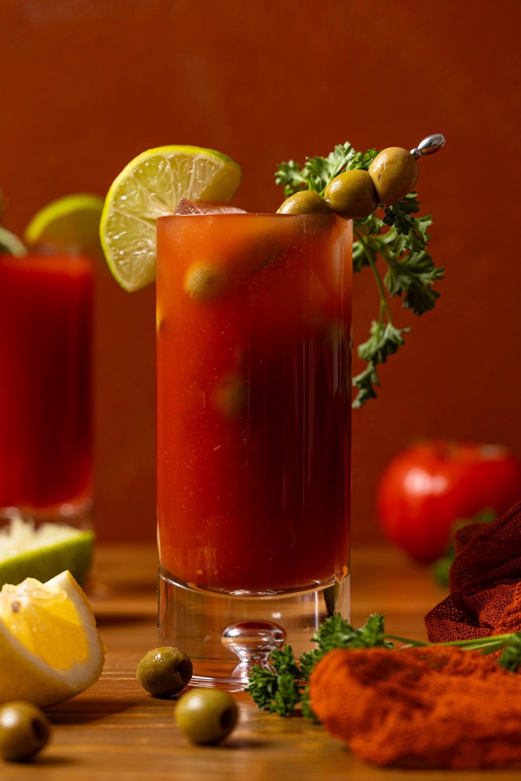 Bloody Mary mocktails in two glasses with lime, olives, parsley, and tomatoes.