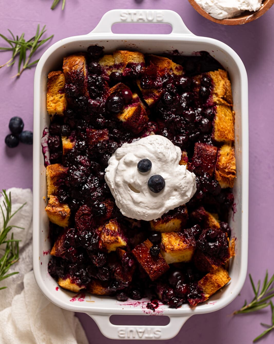 Baking pan of Blueberry Pie French Toast Casserole topped with coconut whipped cream