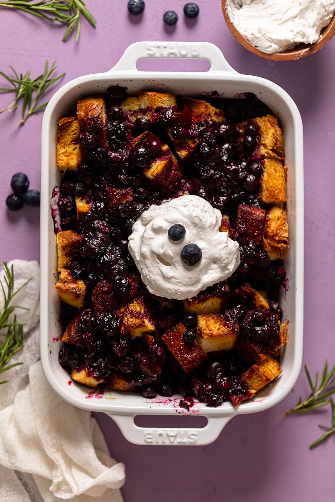 Baking pan of Blueberry Pie French Toast Casserole topped with coconut whipped cream