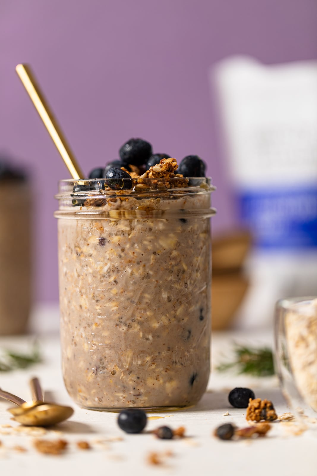 Spoon sticking out of a mason jar of Protein Loaded Blueberry Overnight Oats topped with blueberries