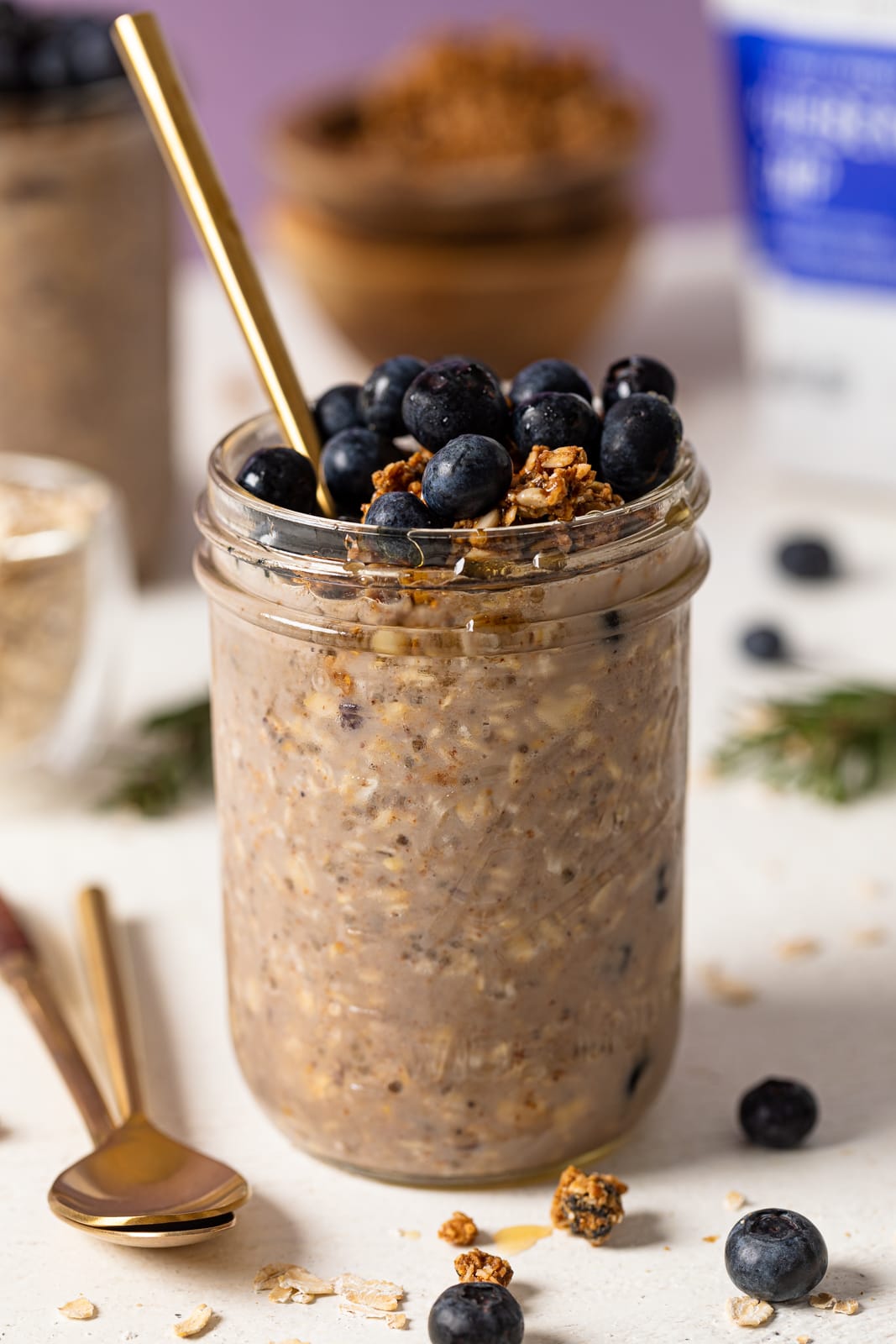 Spoon sticking out of a mason jar of Protein Loaded Blueberry Overnight Oats topped with blueberries