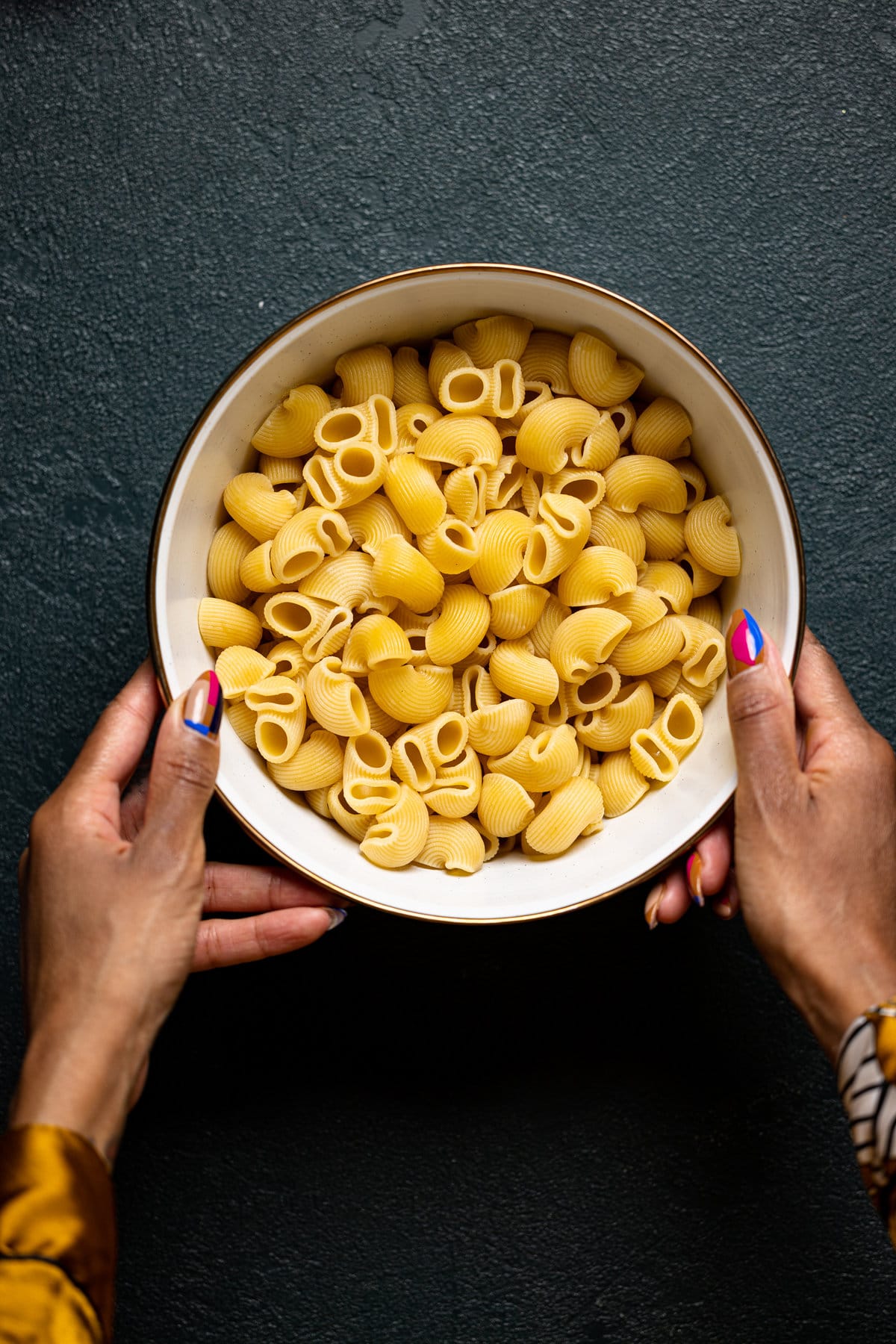 Hands holding a bowl of cooked pasta