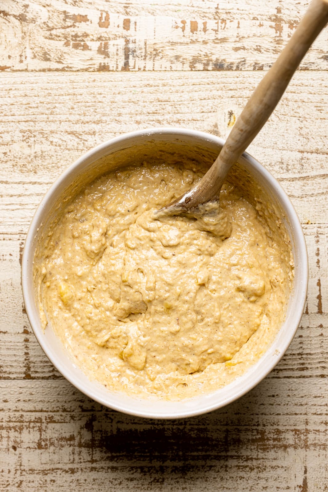 Waffle batter in a bowl with a wooden spoon on a white wood table.