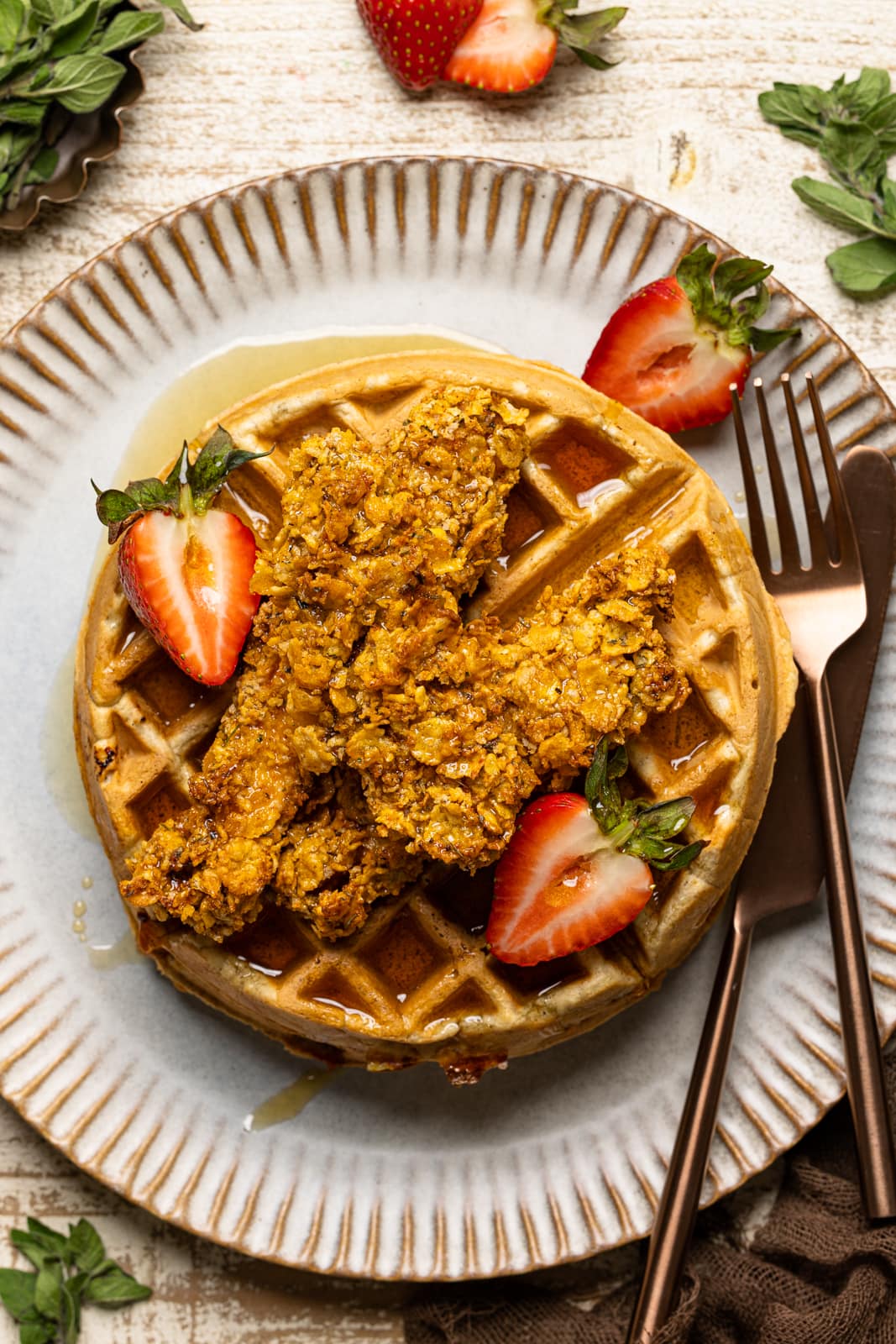 Chicken and waffles on a plate with fork and knife with sliced strawberries. 