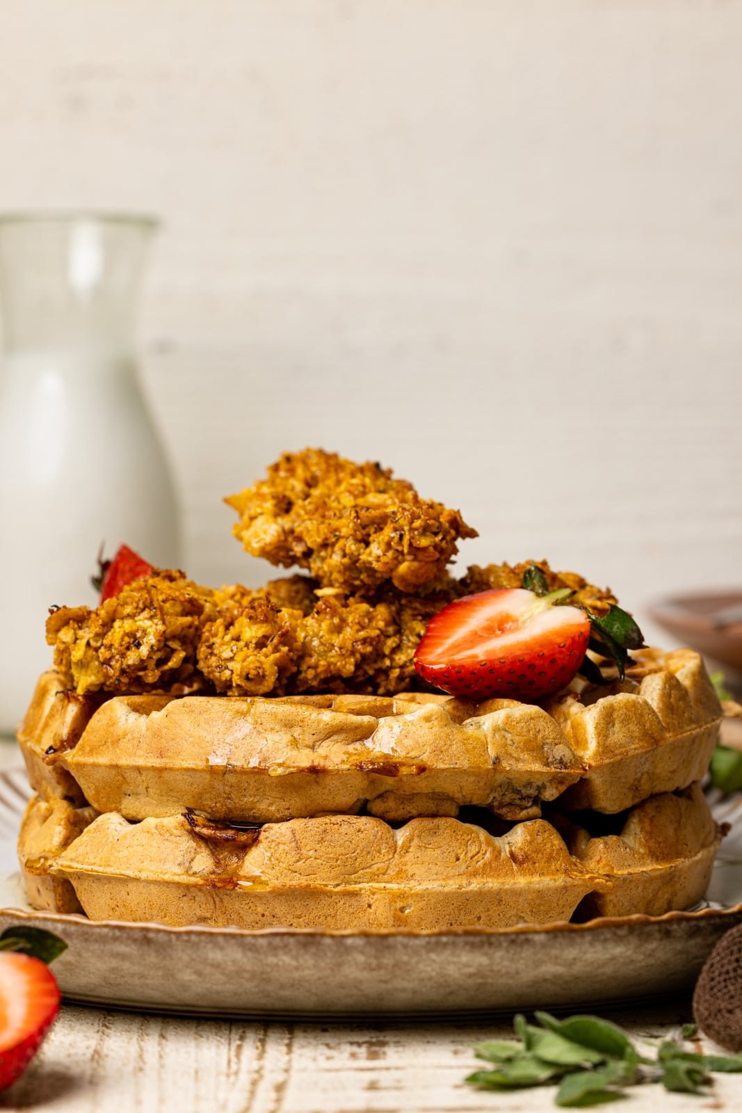 Chicken and waffles on a plate with sliced strawberries and a glass of milk.