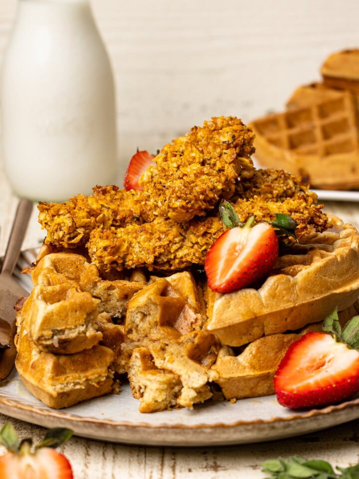 Chicken and waffles on a white plate on a white wood table with a glass of milk and strawberries.