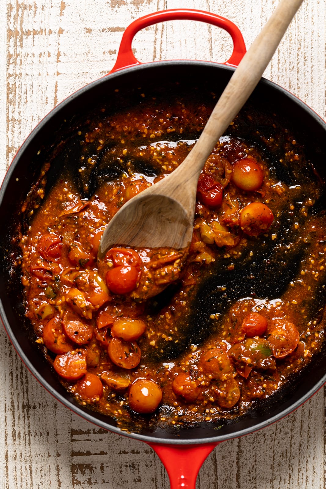 Wooden spoon stirring a skillet of tomatoes and flavorings