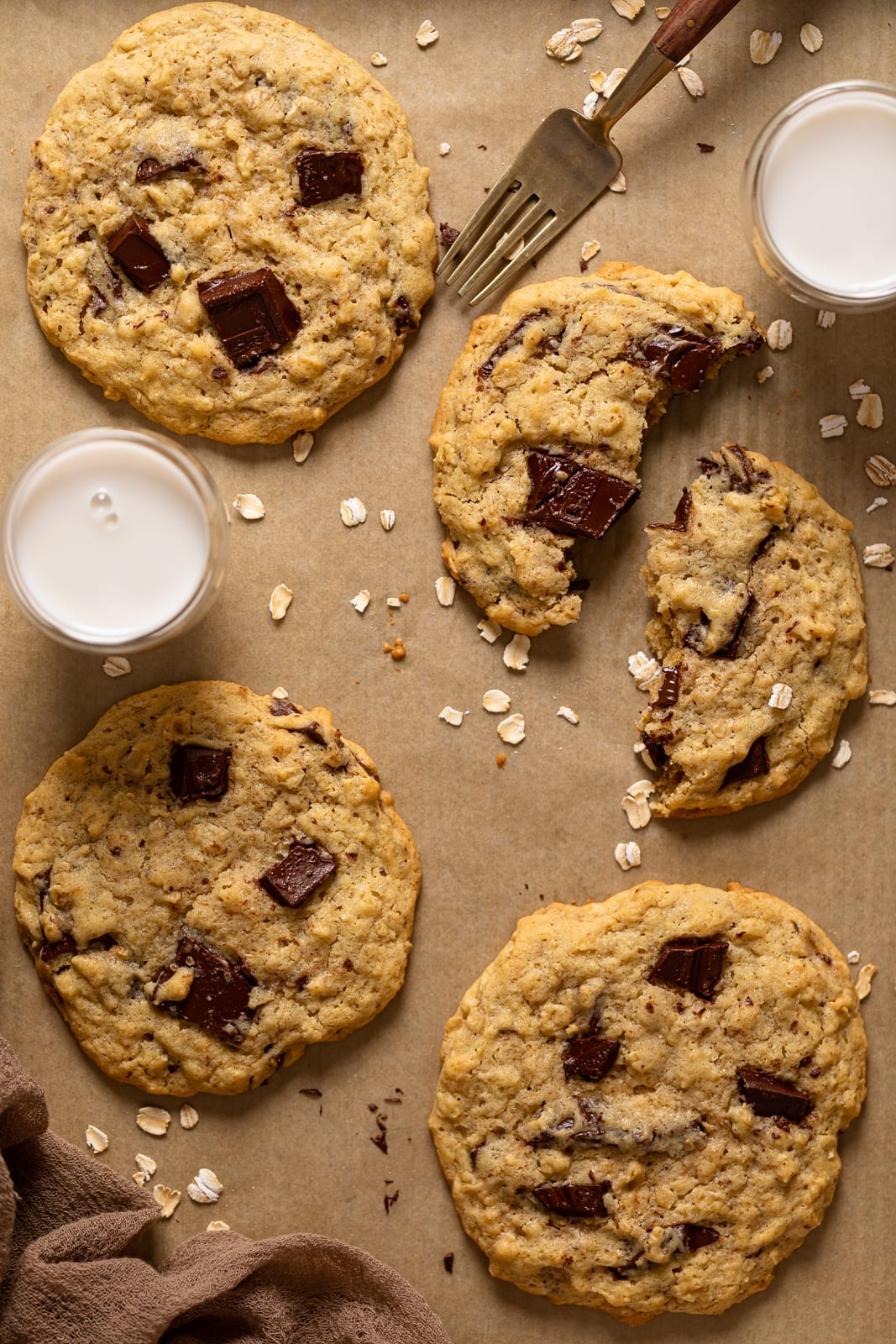 Bakery-Style Oatmeal Chocolate Chip Cookies on parchment paper with one broken in half