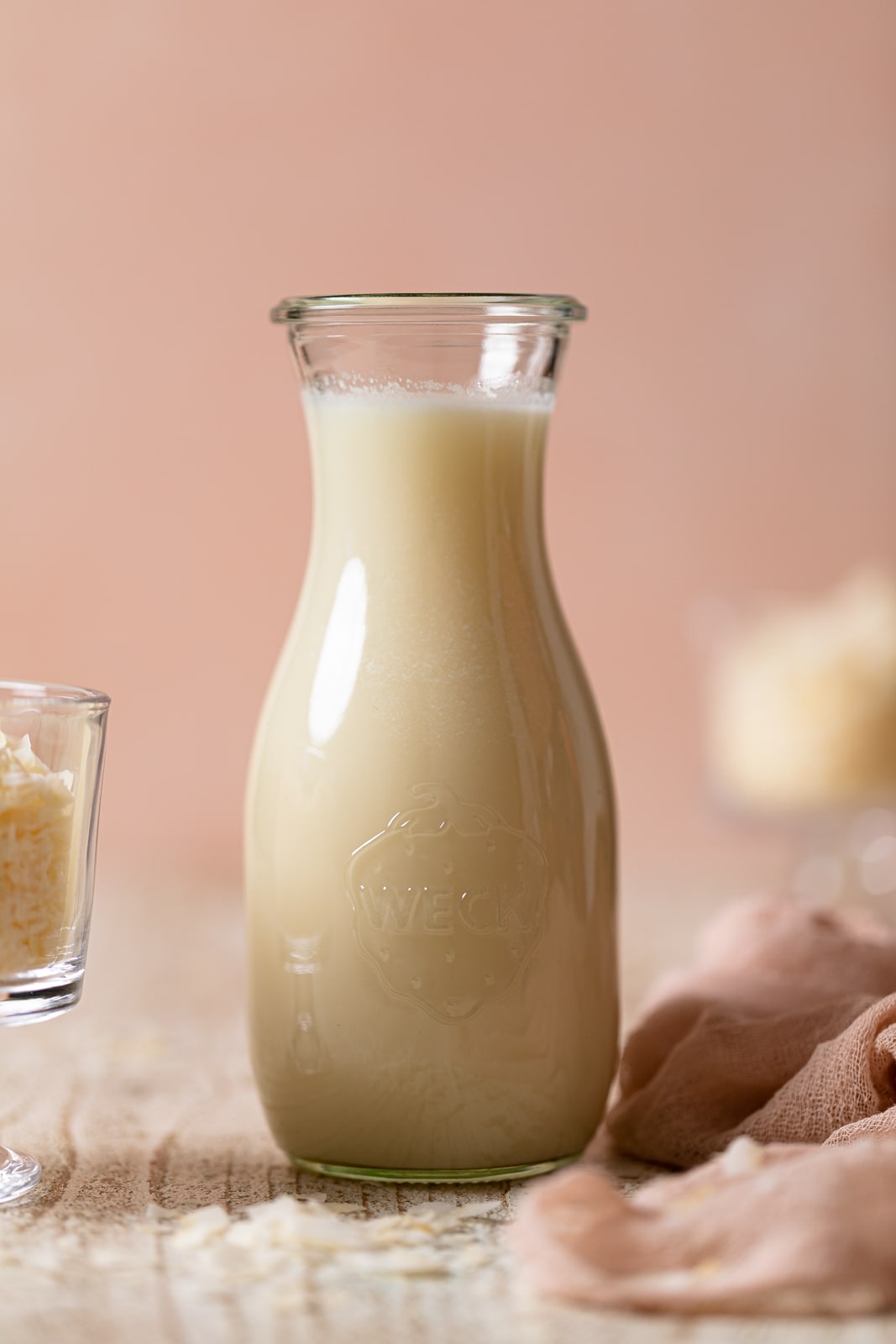 Glass jar of Homemade Coconut Milk against a light pink background