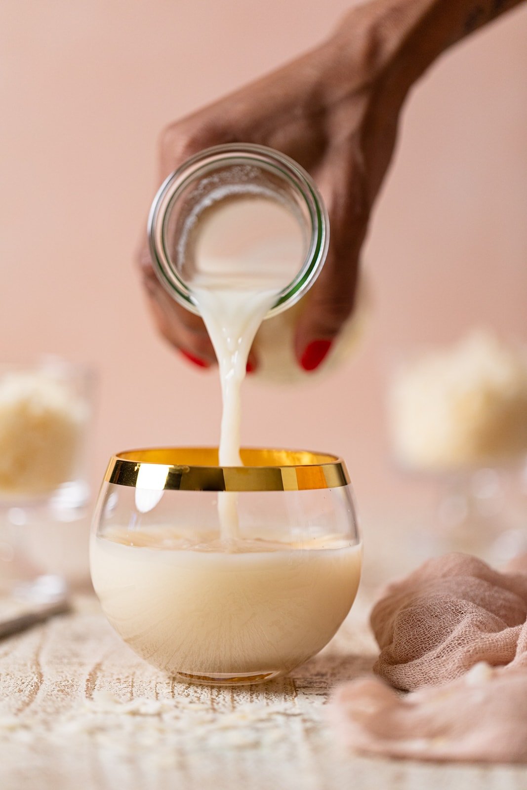Hand holding a jar pouring Homemade Coconut Milk into a gold-rimmed glass