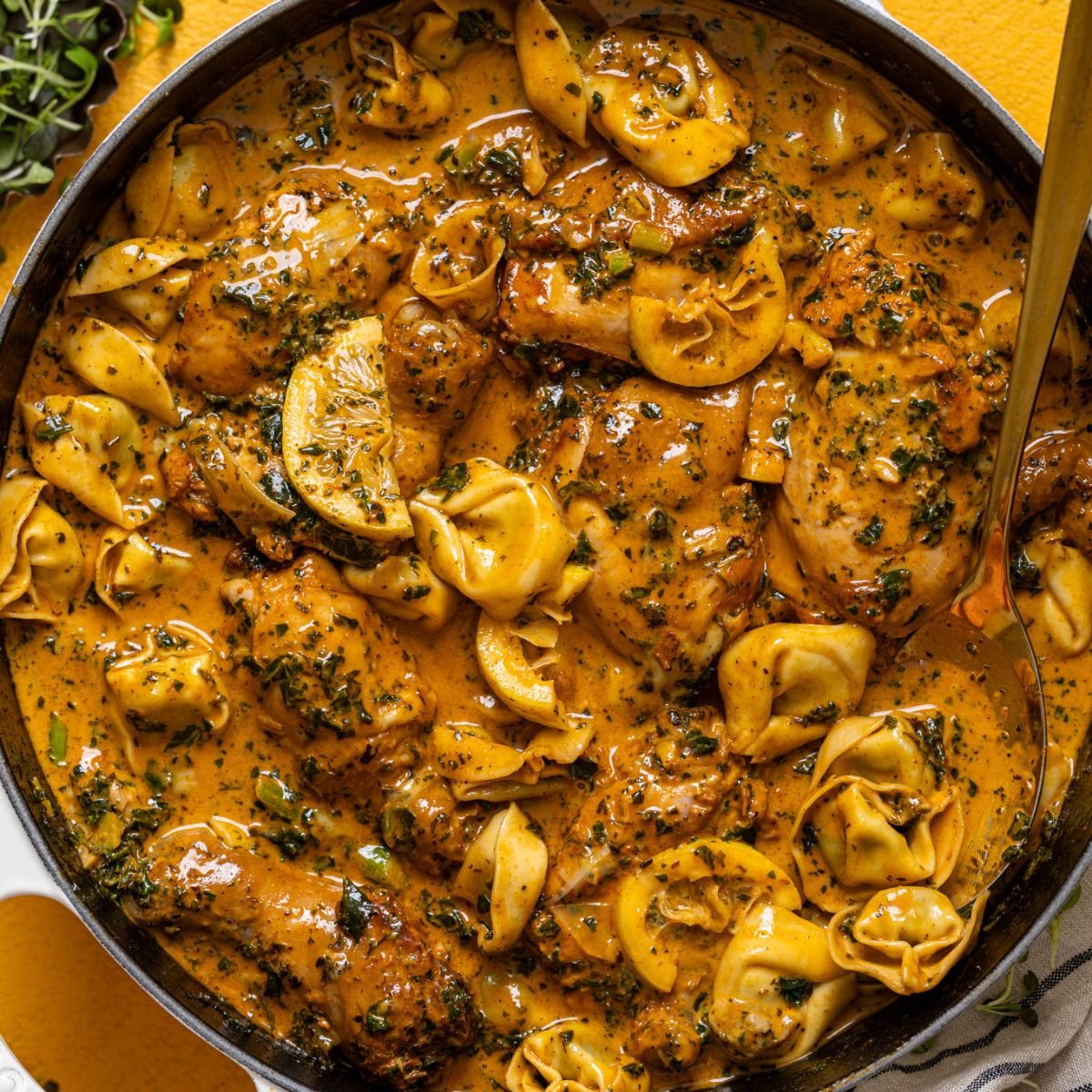 Creamy Lemon Garlic Herb Chicken with Tortellini in a skillet with a spoon.
