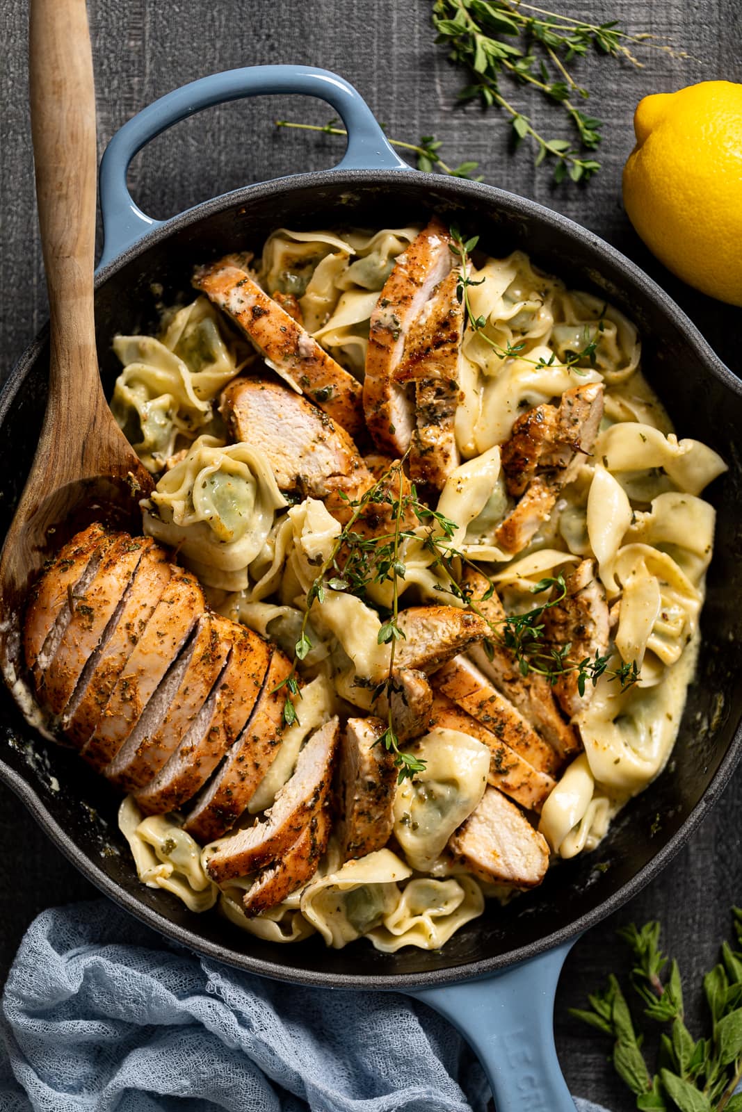 Wooden spoon in a skillet of Creamy Lemon Herb Roasted Chicken with Spinach Tortellini 