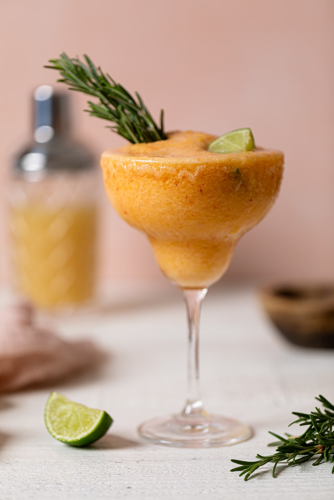 Long-stemmed glass of Frozen Peach Lime Margarita Mocktail topped with a lime wedge and rosemary sprigs