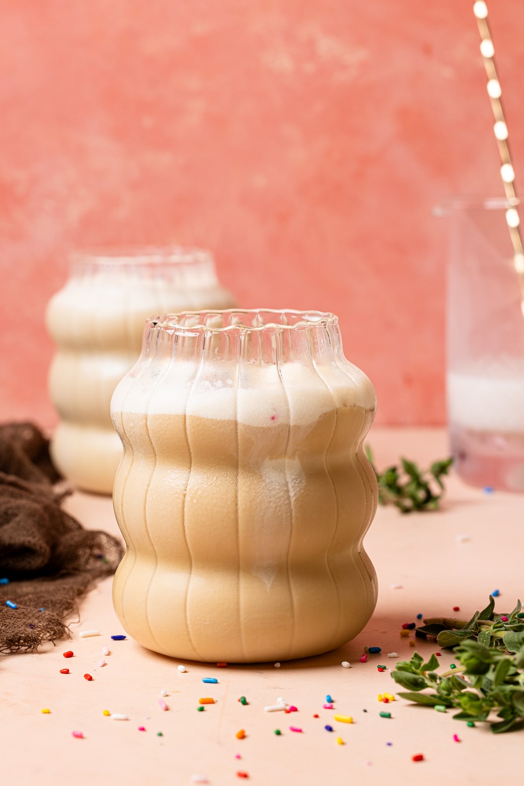 Two glasses of lattes with a glass of milk, sprinkles, and herbs.