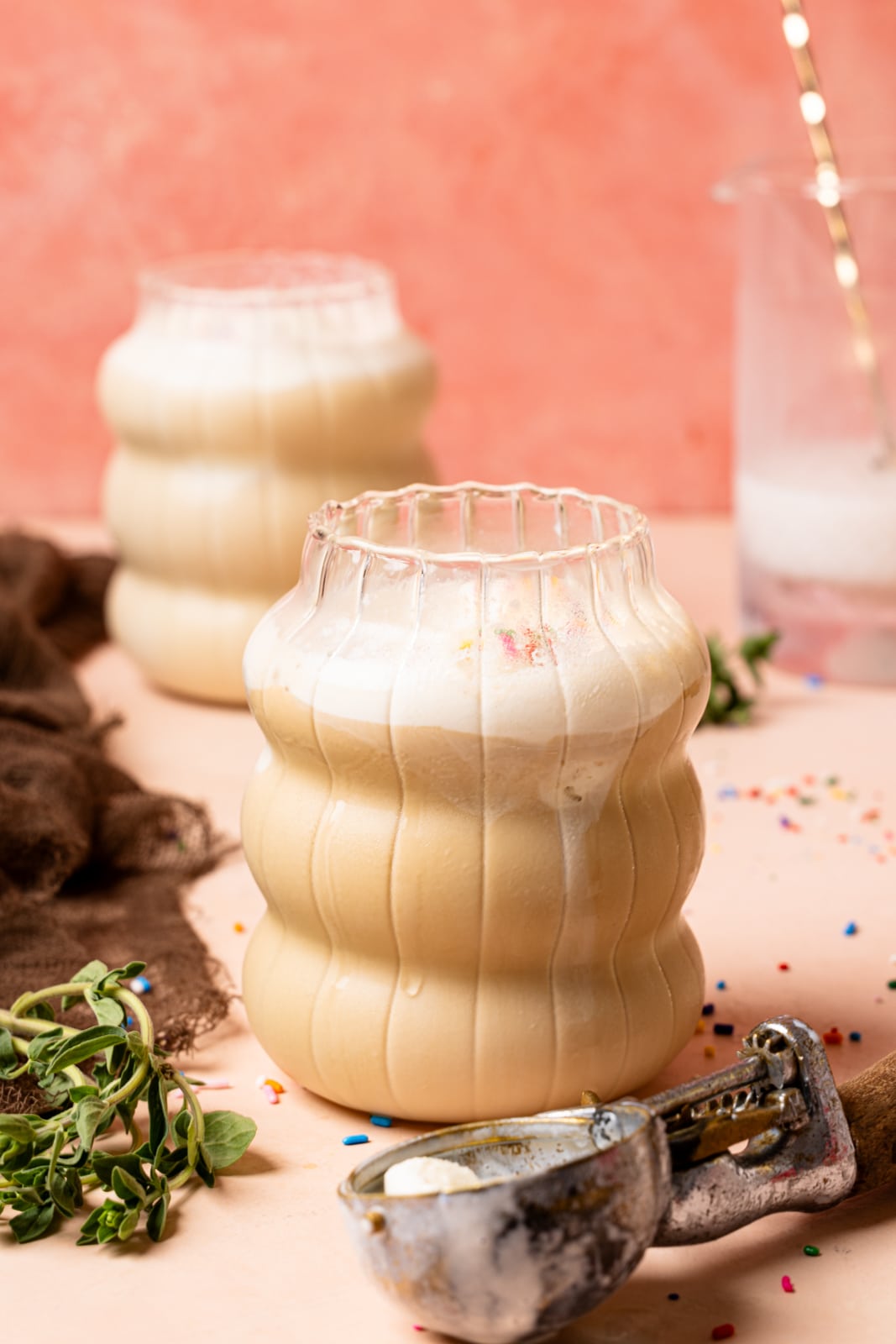 Two glasses of lattes with an ice cream scoop and a glass of milk in the background.