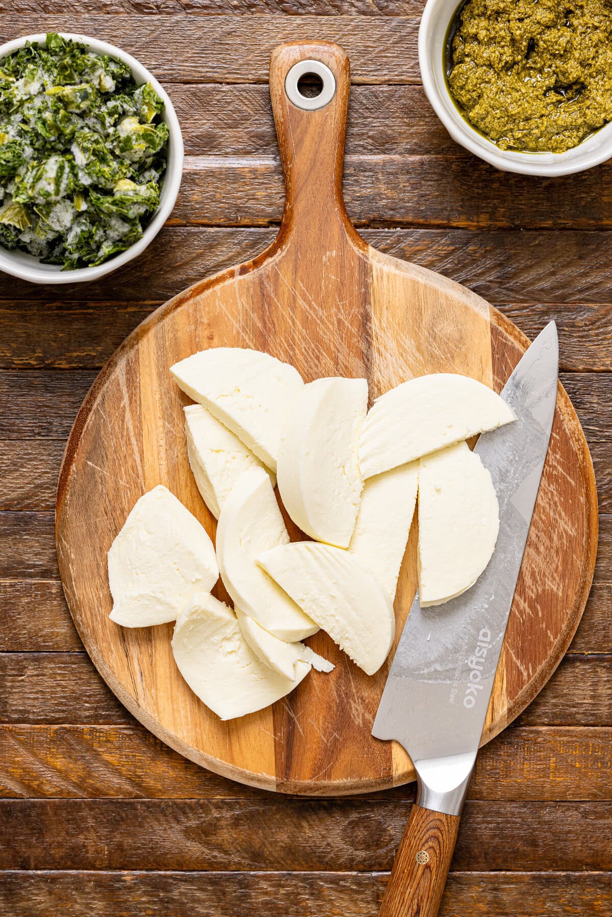 Sliced fresh mozzarella on a cutting board with a knife and pesto.