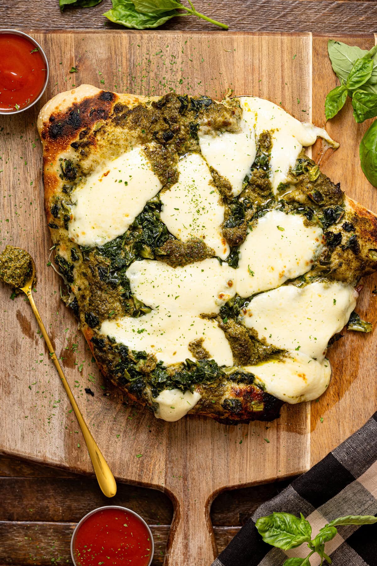 Cooked pizza on a cutting board with sauces and a spoon.