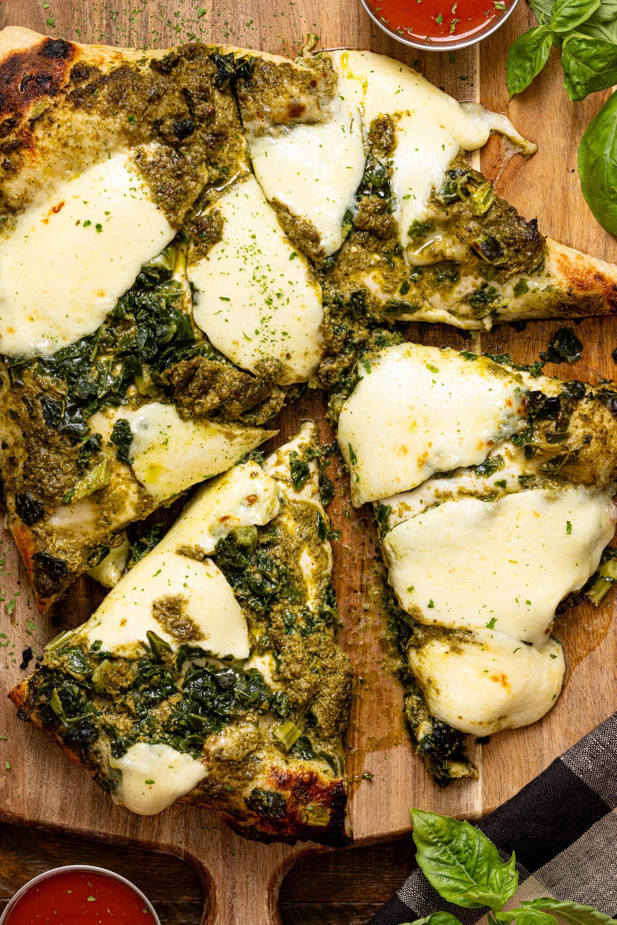 Kale pizza on a cutting board with basil and sauce.