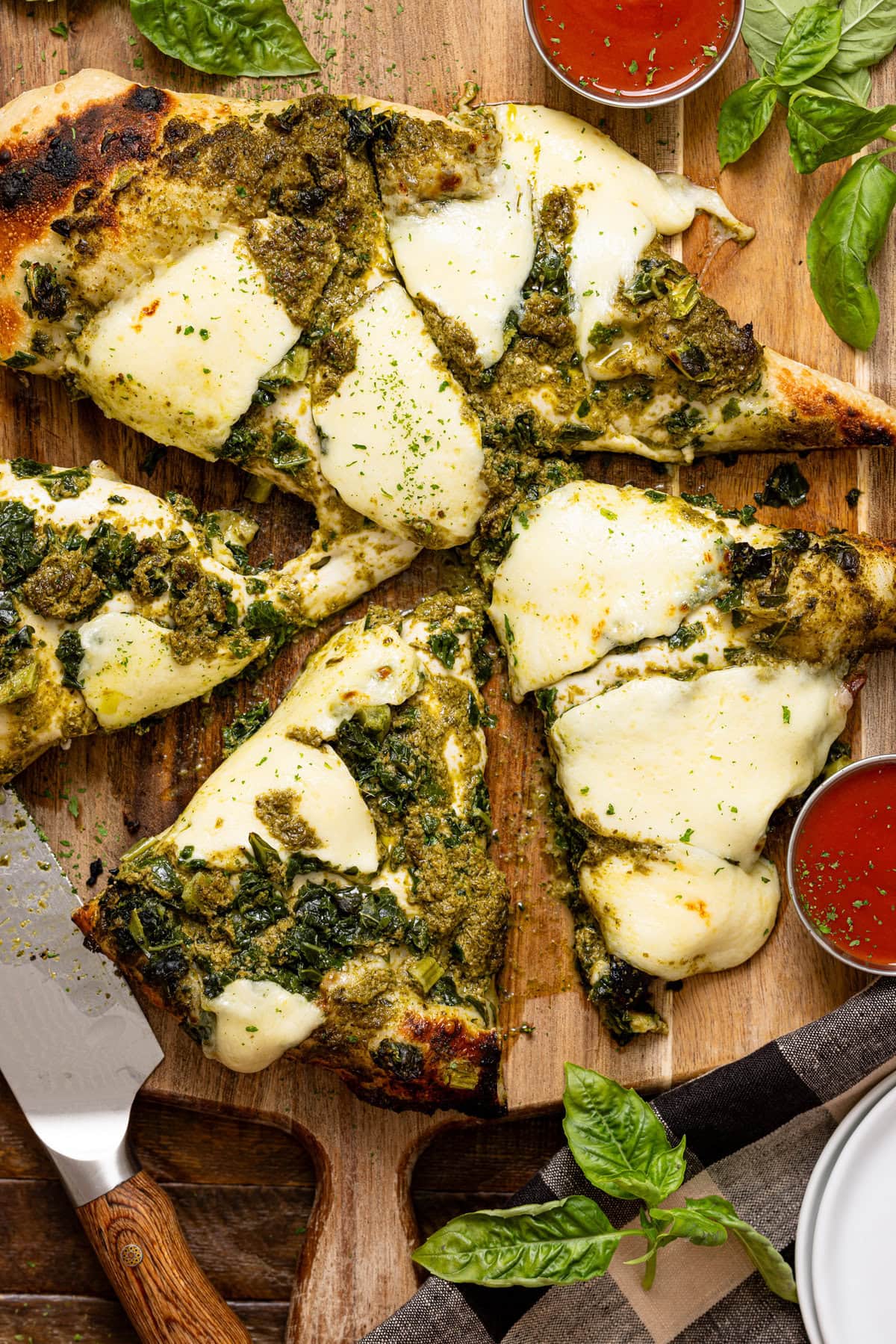 Sliced pizza with a knife, sauces, and basil leaves. 