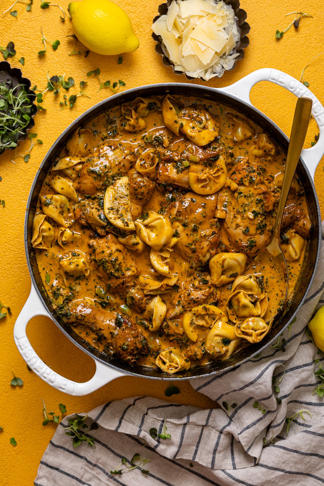Creamy Lemon Garlic Herb Chicken with Tortellini in a skillet with parmesan and garnish.