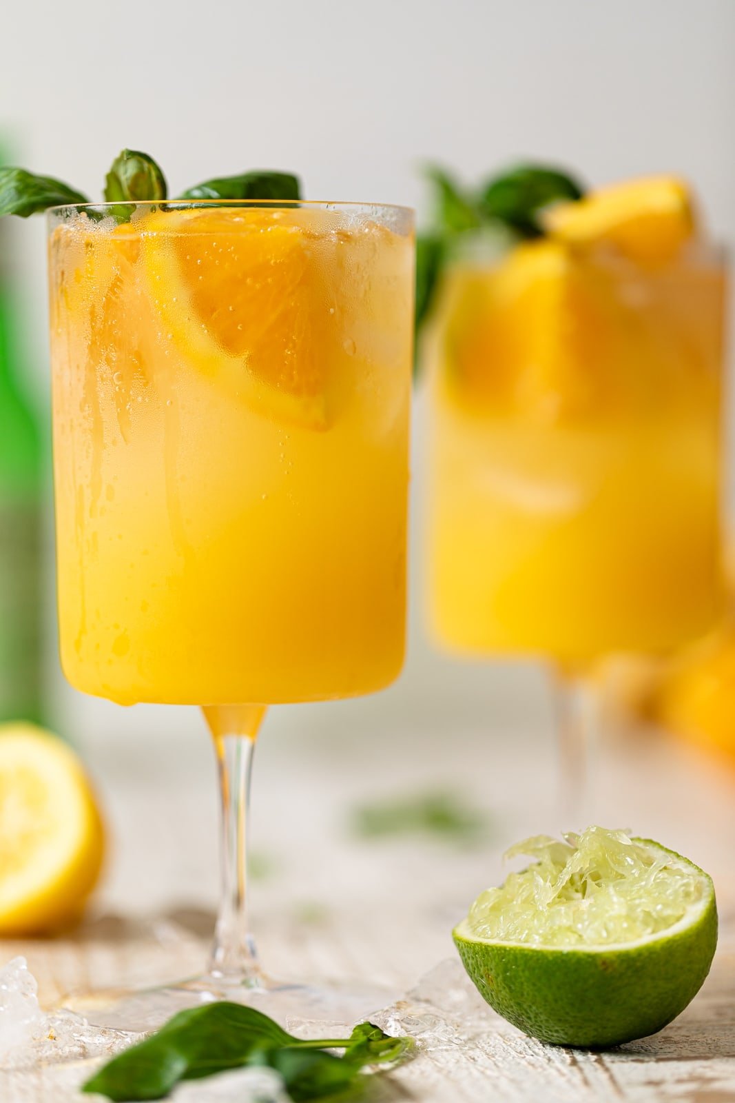 Bright Orange Crush Mocktail with Basil in a long-stemmed glass next to basil leaves and a lime