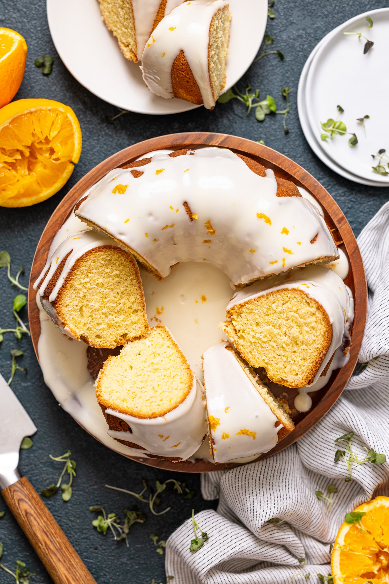 Orange Olive Oil Bundt Cake on a cake stand with oranges and a knife.