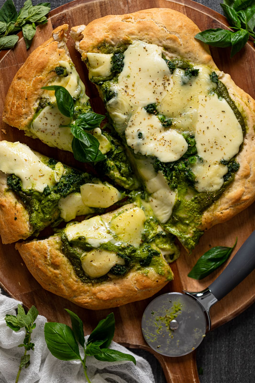 Half-sliced Kale Pesto Pizza with a pizza cutter