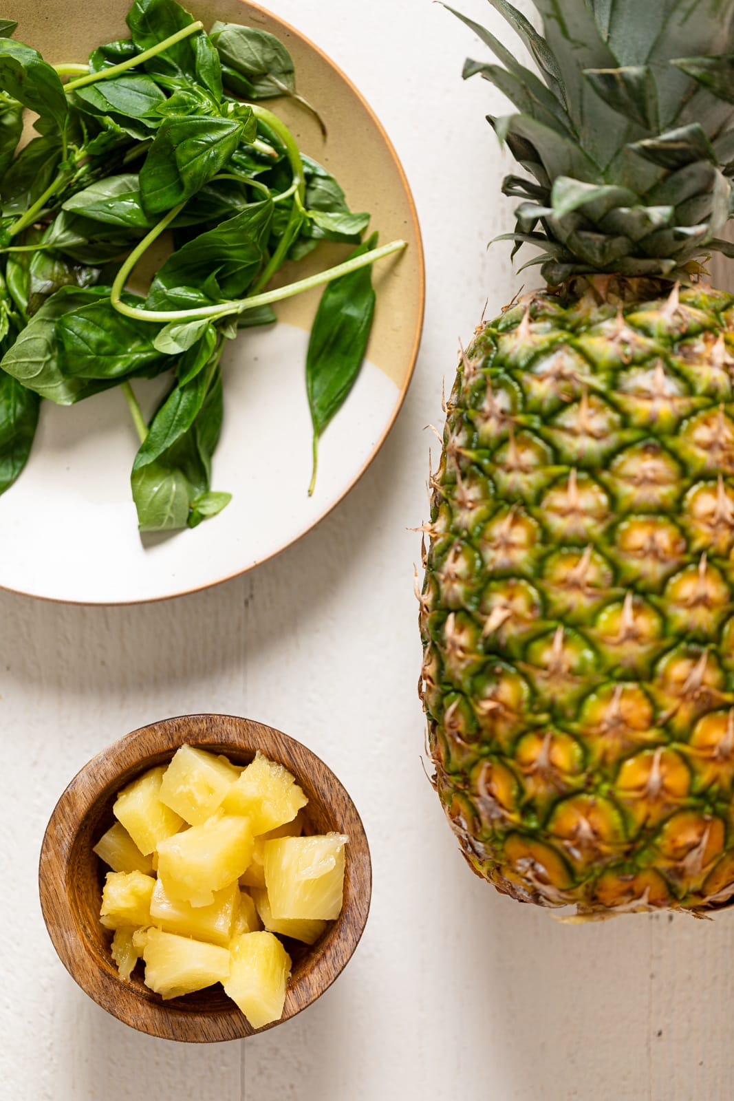 A whole pineapple, pineapple chunks, and basil leaves