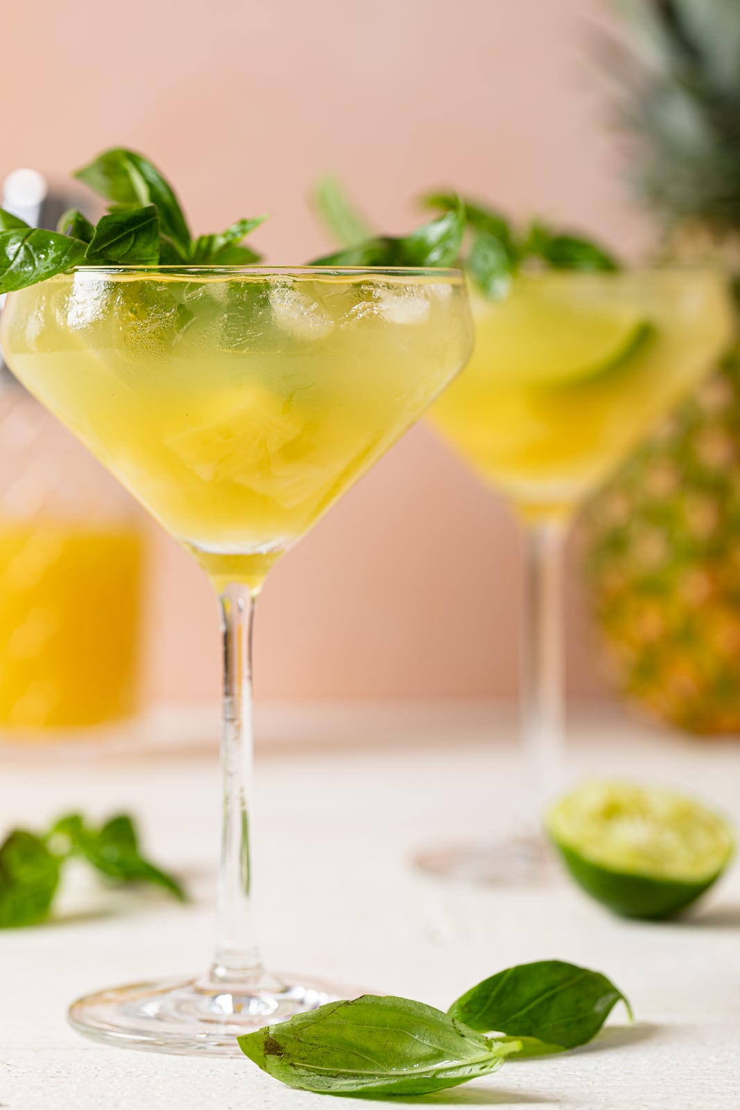 Two long-stemmed glasses of Pineapple Coconut Basil Mocktail with Lime topped with basil leaves