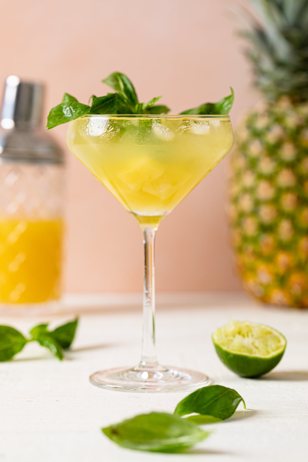 Long-stemmed glass of Pineapple Coconut Basil Mocktail with Lime topped with basil leaves