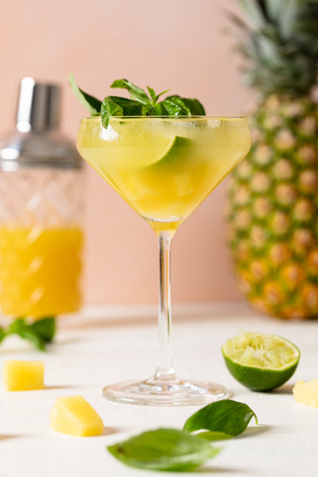 Long-stemmed glass of Pineapple Coconut Basil Mocktail with Lime topped with basil leaves and a lime wedge