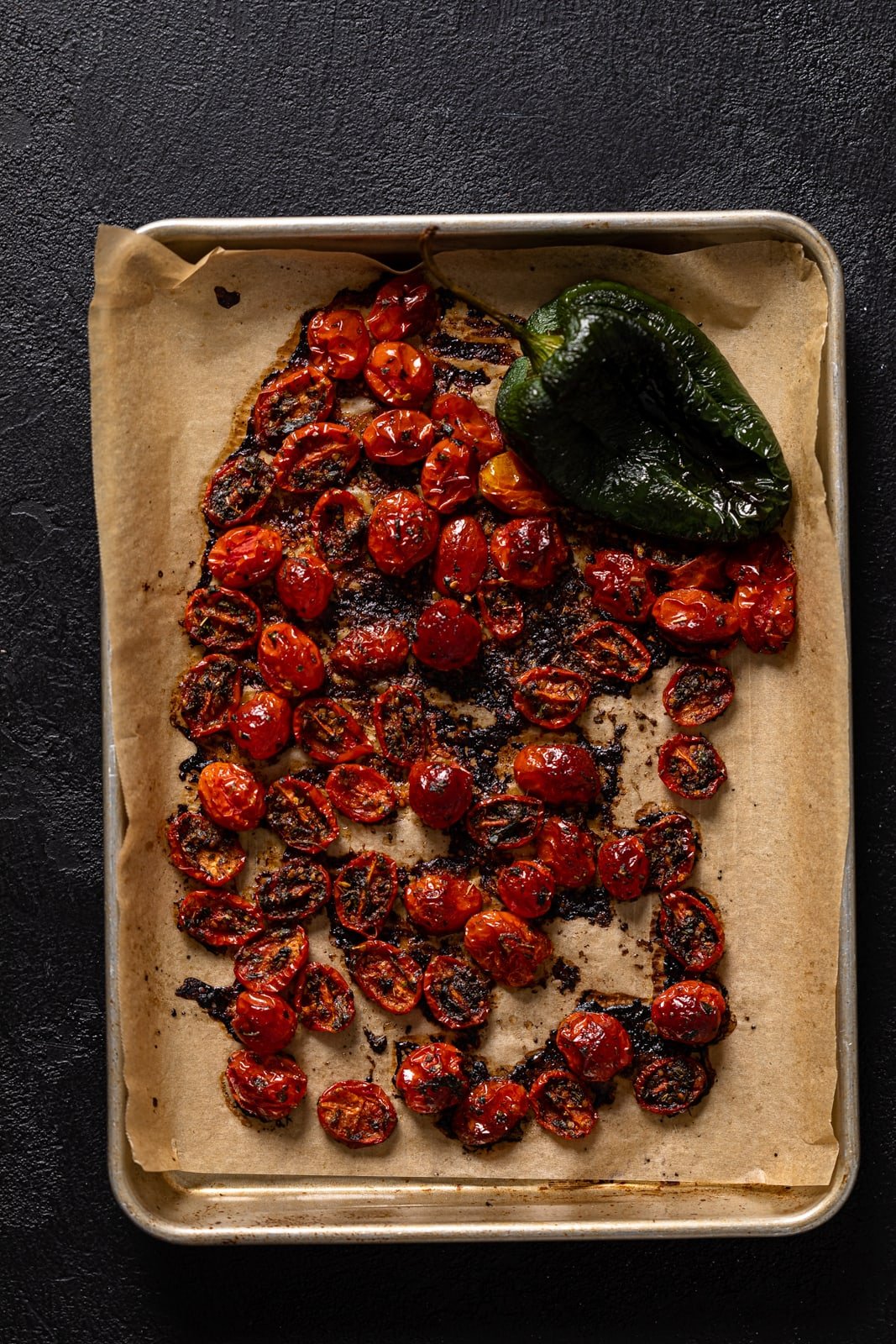 Roasted tomatoes and a pepper on a baking sheet