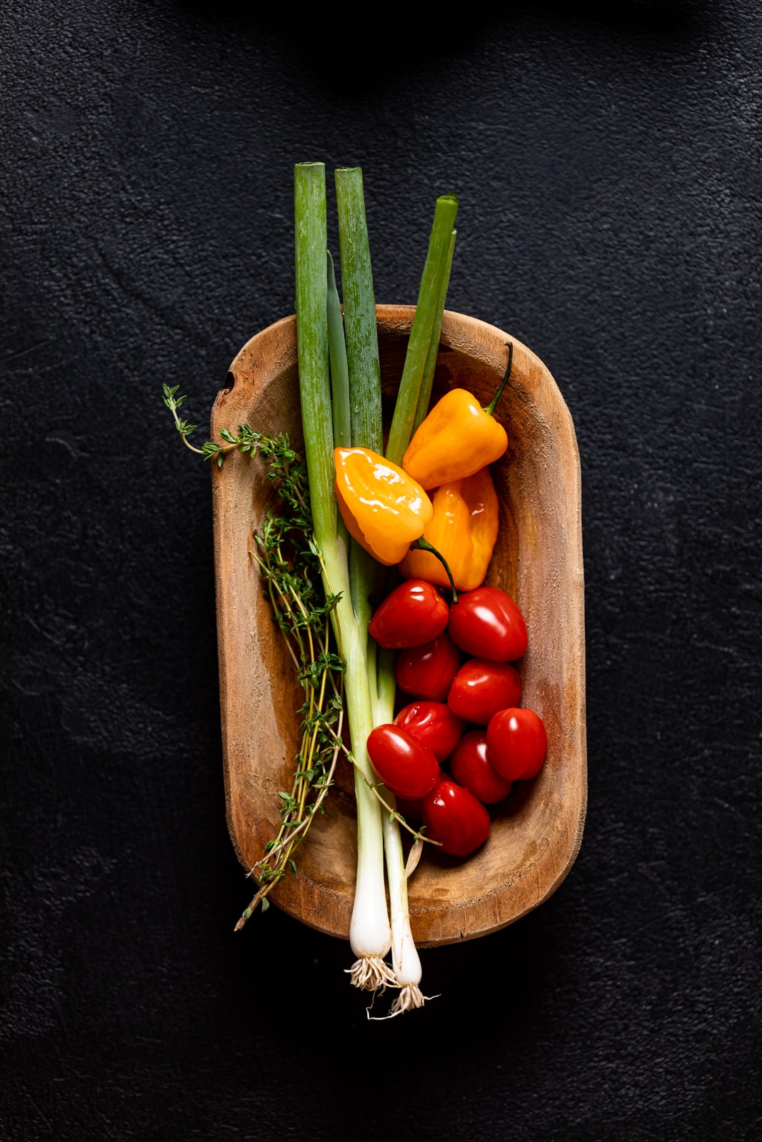 Wooden bowl of green onions, peppers, tomatoes, and thyme