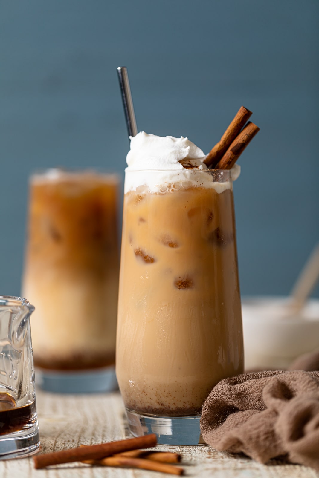 Tall glass full of a Dirty Chai Maple Iced Latte topped with coconut whipped cream and cinnamon sticks