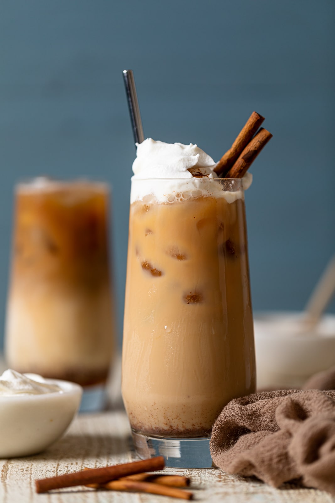 Tall glass full of a Dirty Chai Maple Iced Latte topped with coconut whipped cream and cinnamon sticks