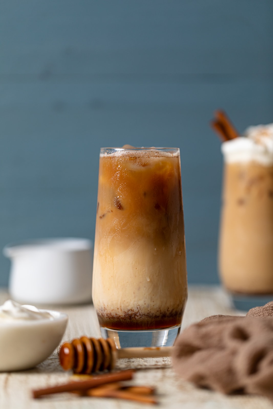 Tall glass of a Dirty Chai Maple Iced Latte with a honey dipper