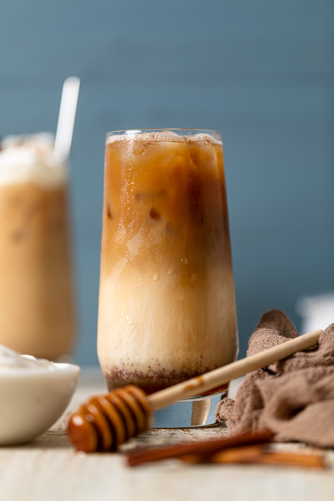 Tall glass full of a Dirty Chai Maple Iced Latte with a honey dipper