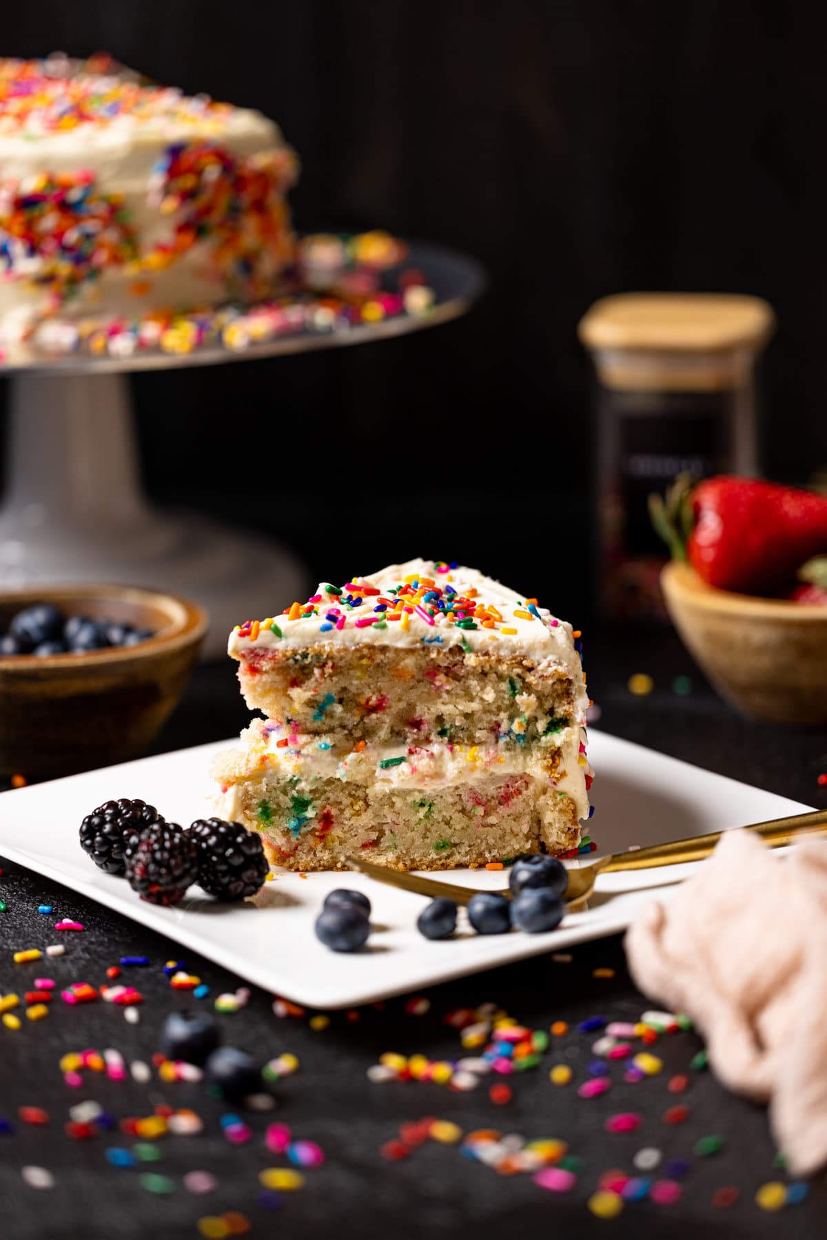 Slice of Vegan Funfetti Cake with Vanilla Buttercream near berries