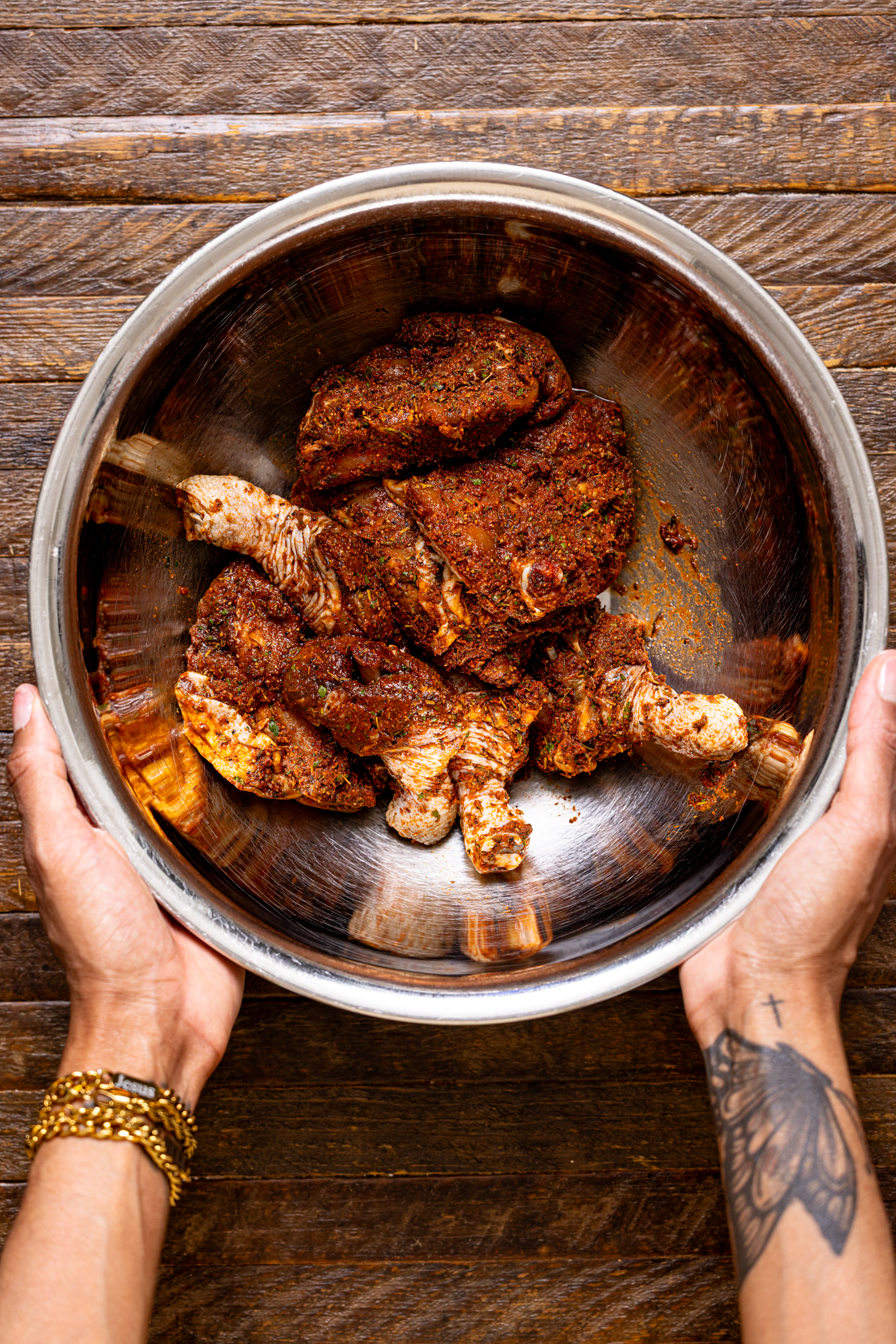 A silver bowl being held by woman hands with marinated chicken.