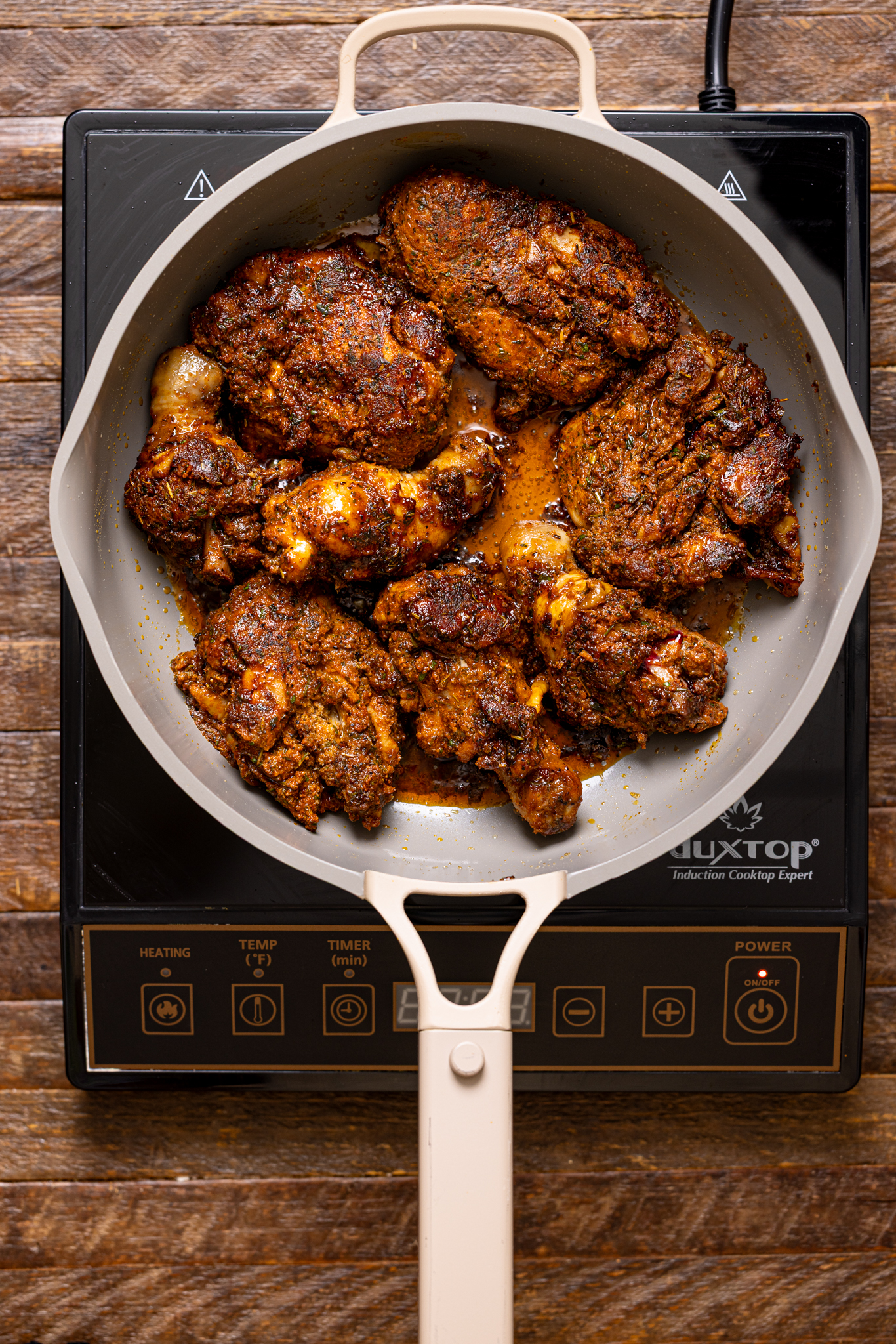 Brown stew chicken being seared in a skillet over the stovetop.