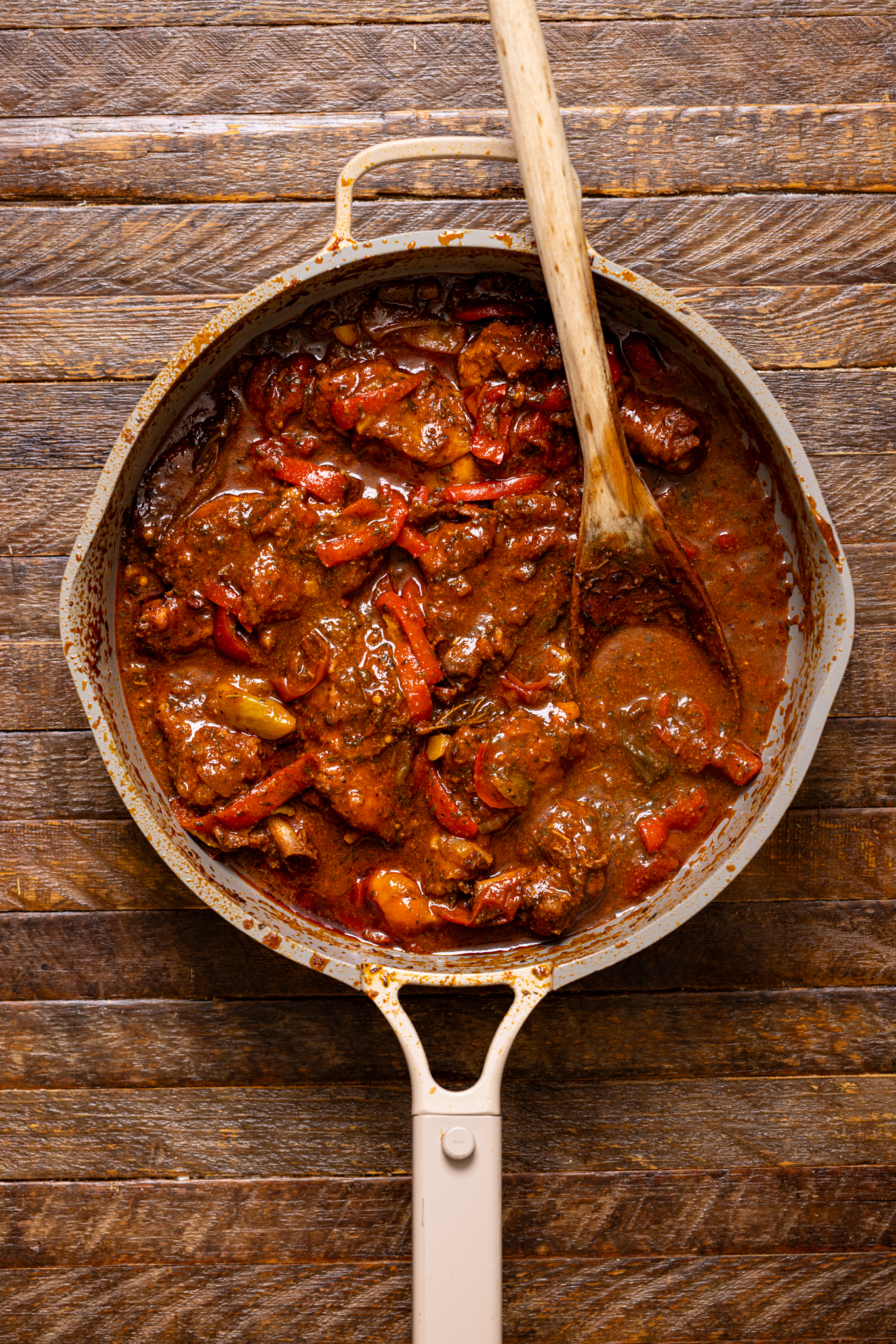 Jamaican Brown Stew chicken cooked in a skillet with a wooden spoon.