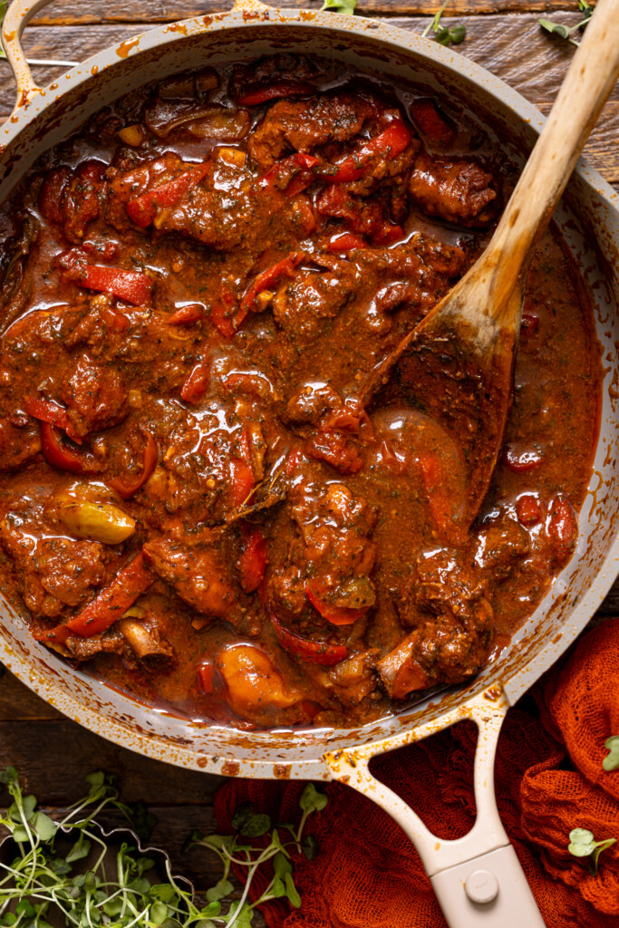 Up close shot of Jamaican Brown Stew Chicken with a wooden spoon.