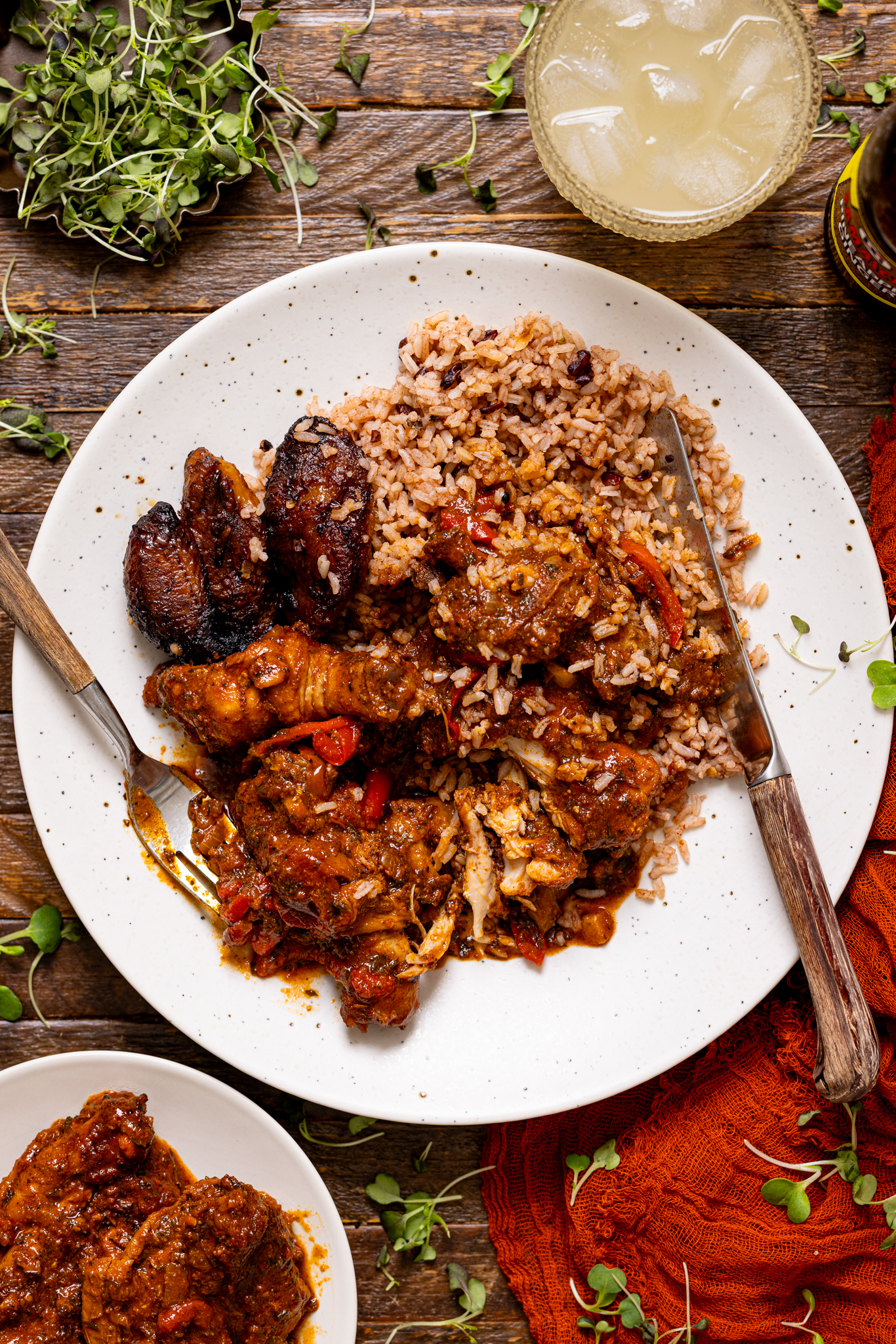 An image of a plate of stew chicken with rice and peas and fried plantain with forks. 