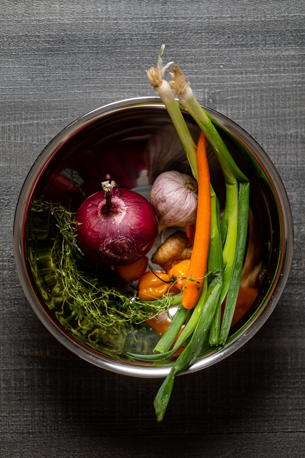 Bowl of produce including red onion, green onion, carrots, and garlic