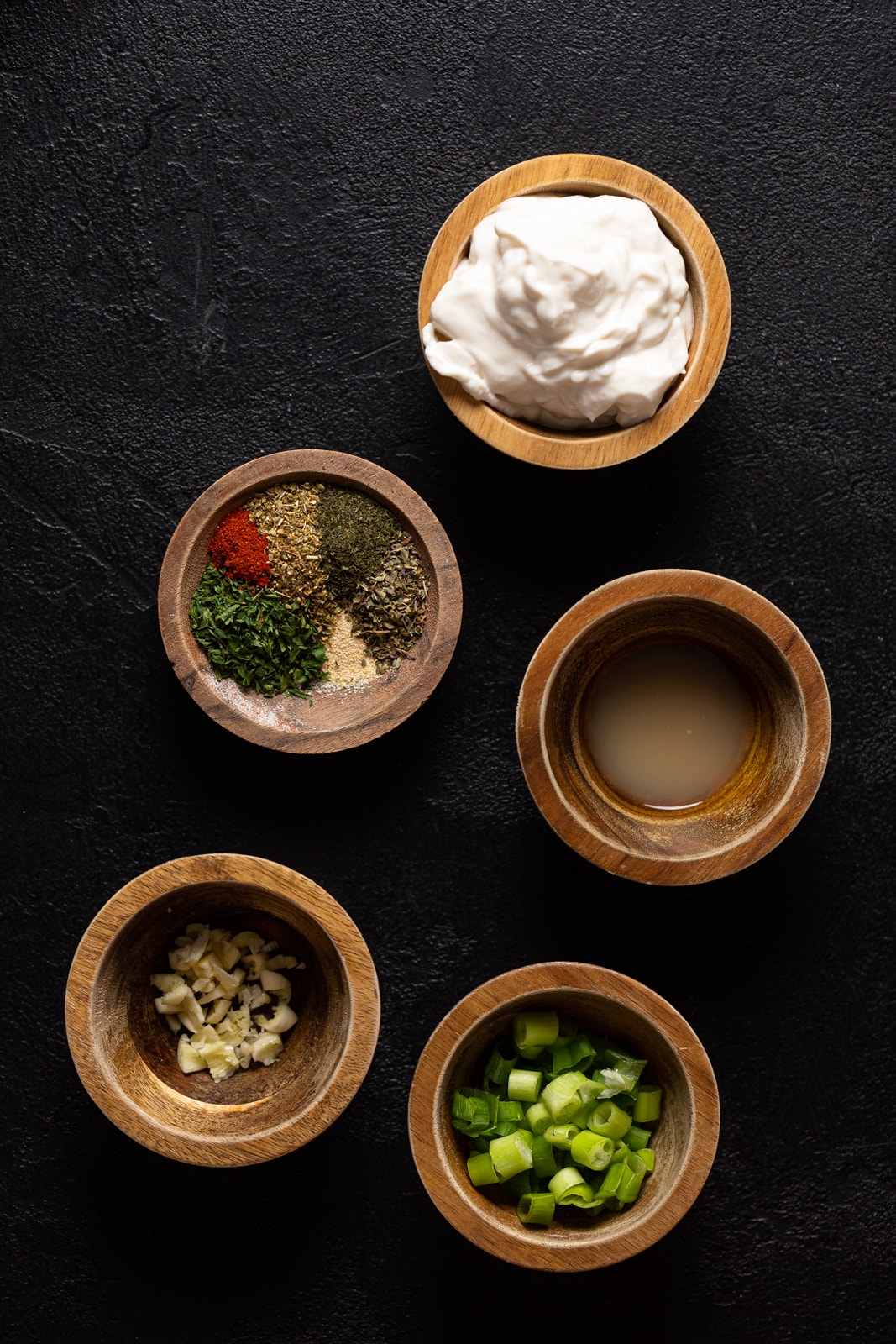 Small, wooden bowls of ingredients including green onion, garlic, and spices