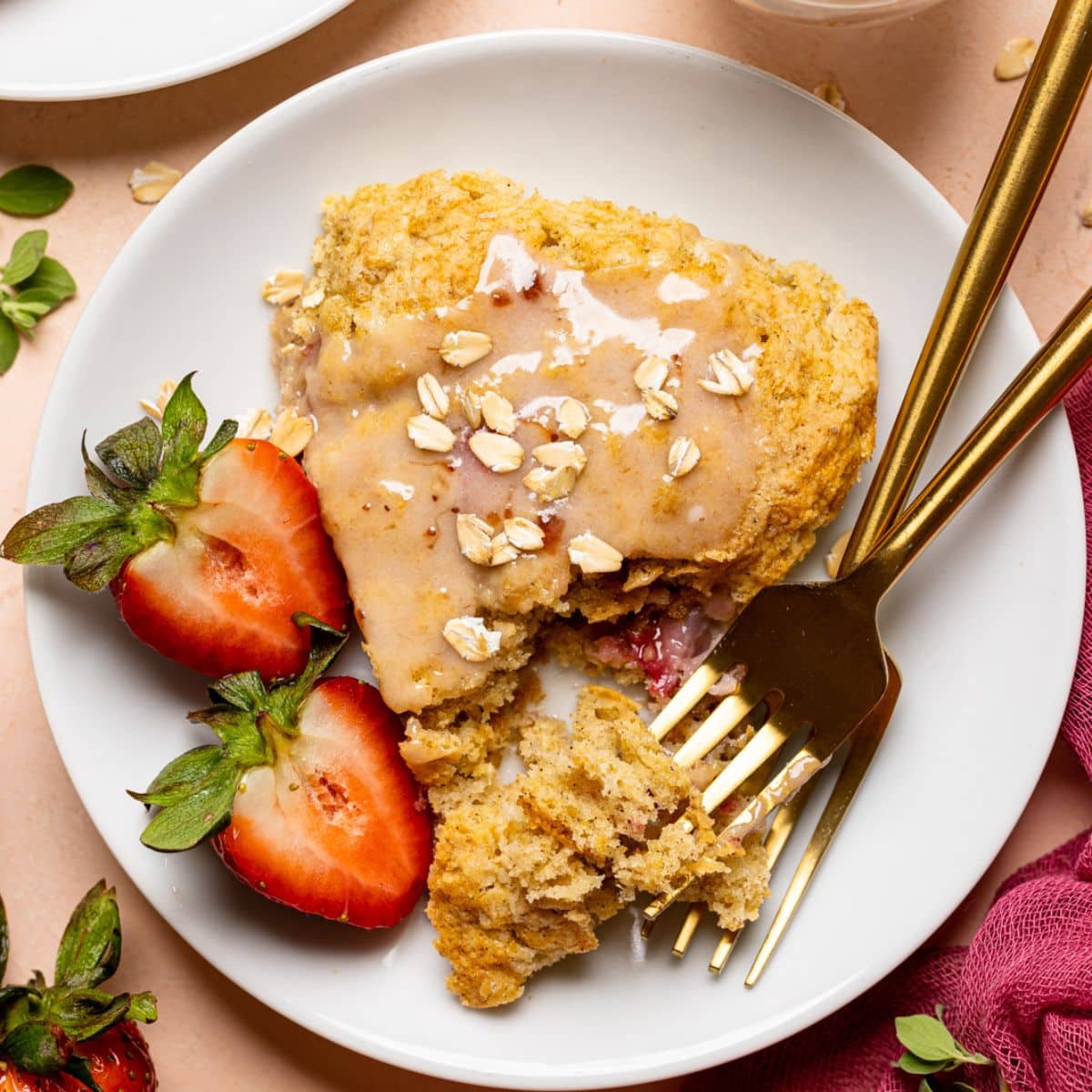 Baked scones on a white plate with two forks and sliced strawberries.